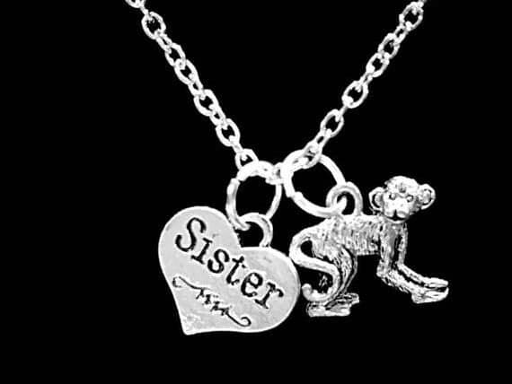 Silver necklace with a heart charm that says sister in black font and a monkey charm. 