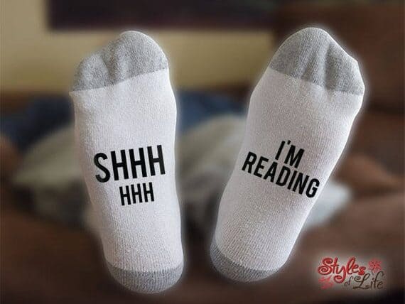 Bottom of white socks with grey tips with black font that says "SHHHHH" one one and "I'm reading" on the other.
