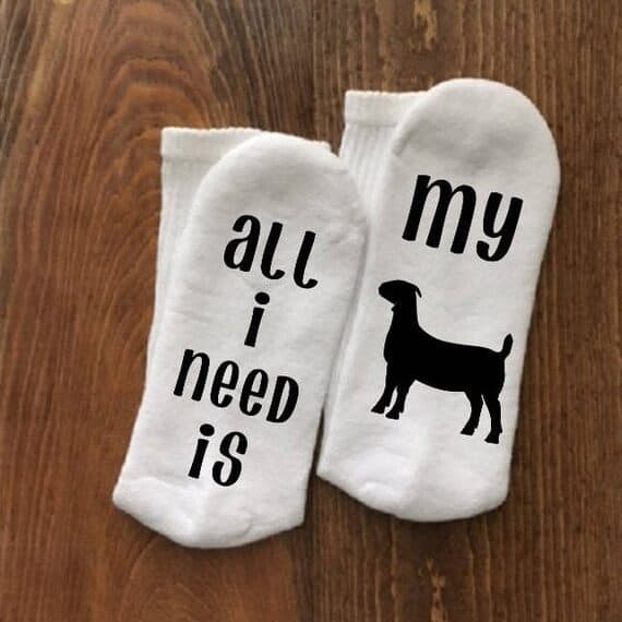 White socks with black font one that says All I need is and the other My and a silhouette of a goat.