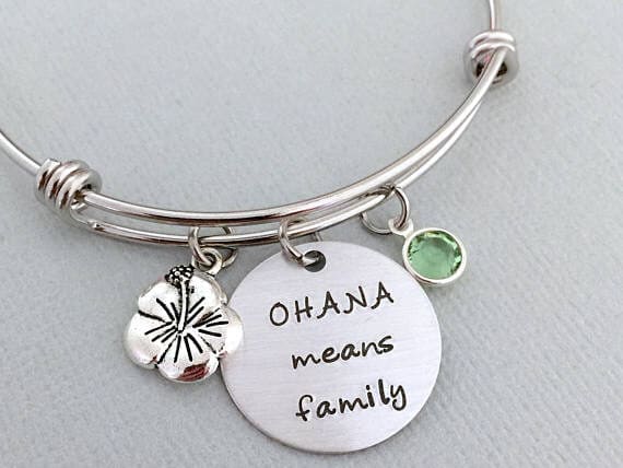 Mother's day gifts for sister-in-laws include this adorable bracelet. Silver bracelet with a round charm that says OHANA means family, a tropical flower charm and a green charm. 