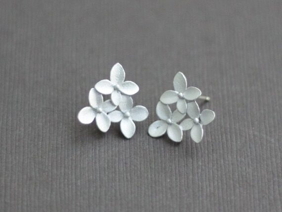 Two studded earrings each with three white flowers on them. 