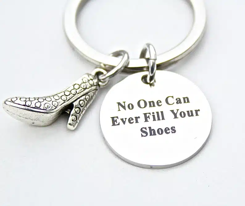 Silver keychain with a round charm that says "no one can fill your shoes" and a high heel charm beside it. 