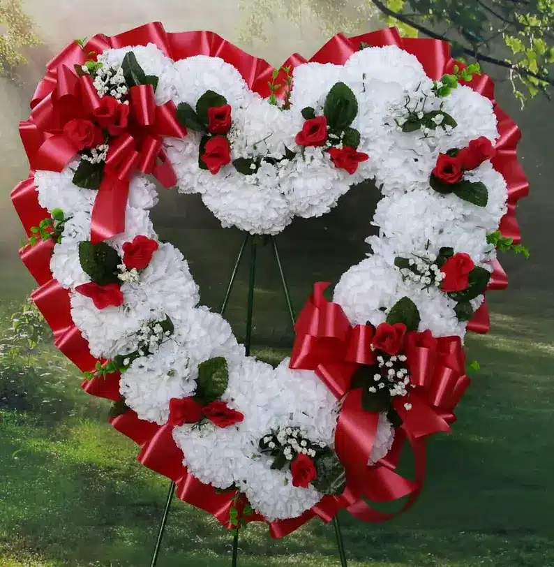 Heart wreath with red ribbon all around and white flowers. 