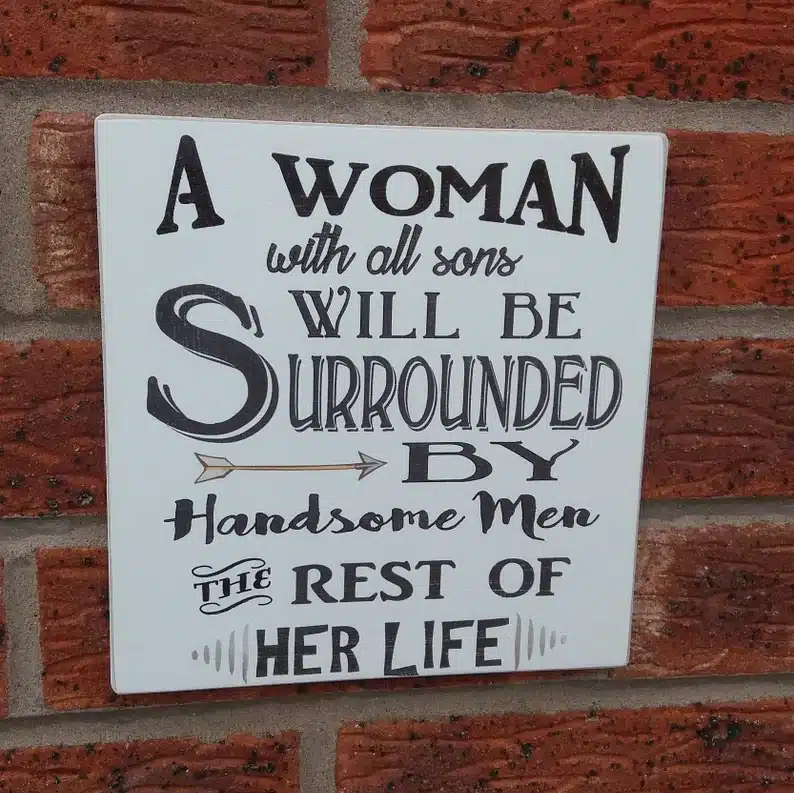 White square board with black font that says "a woman with all sons will be surrounded by handsome men the rest of her life" 