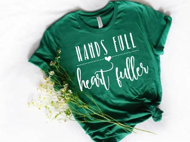 Dark green t-shirt with white font that says hands full, heart fuller"