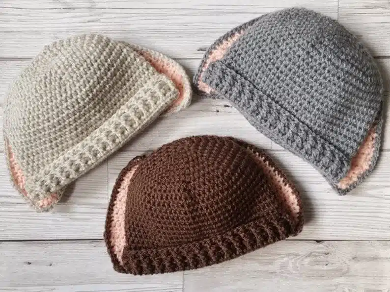 Three crocheted bunny baby hats shown, light grey, grey, and brown. 