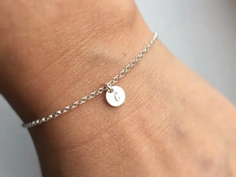 Mother’s Day Gifts for Sister-in-Laws: close up of a woman's wrist with a thin silver chain and a small round charm with a C on it. 