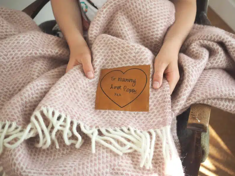 Tan colored personalized woolen throw blanket, small brown patch with a black heart where you can add your own writing. 