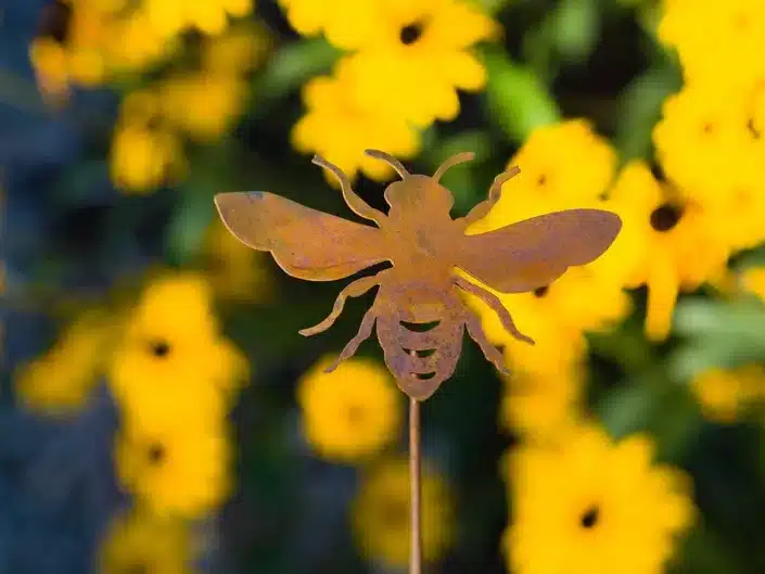 Mother’s Day Gifts for Gardeners: Bronze colored metal garden stake shaped like a honey bee with yellow flowers blurred in the background. 