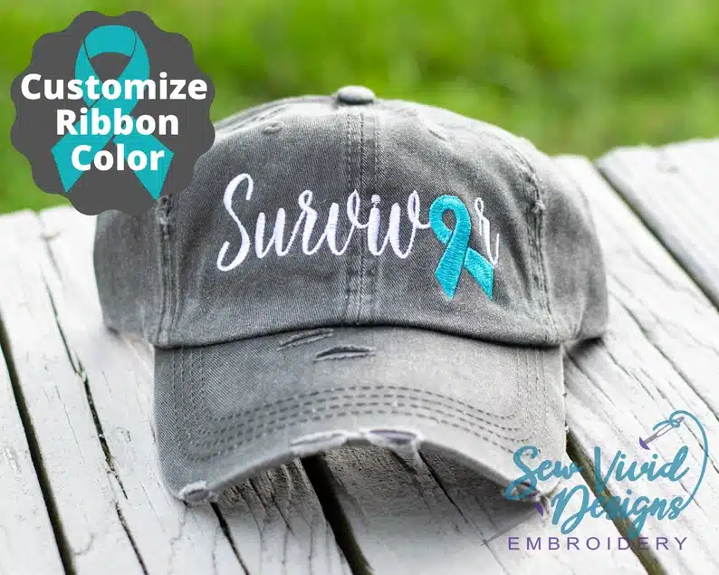 Grey baseball hat that sat says survivor in white stiches and a teal colored ribbon.  