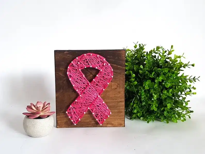 Wooden square sign with a pink breast cancer symbol made of strings on it. 