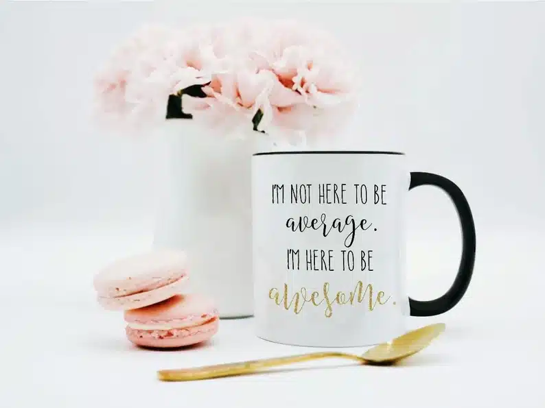 White coffee mug with a black handle that says "I'm not here to be average. I'm here to be awesome" in black font. 