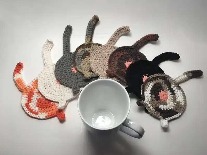 Eight cat butt coasters all different colors and a white coffee mug. 