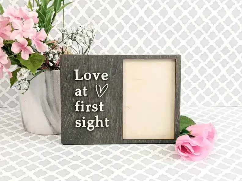 Wooden grey frame with white stick out letters that says Love at First sight. 