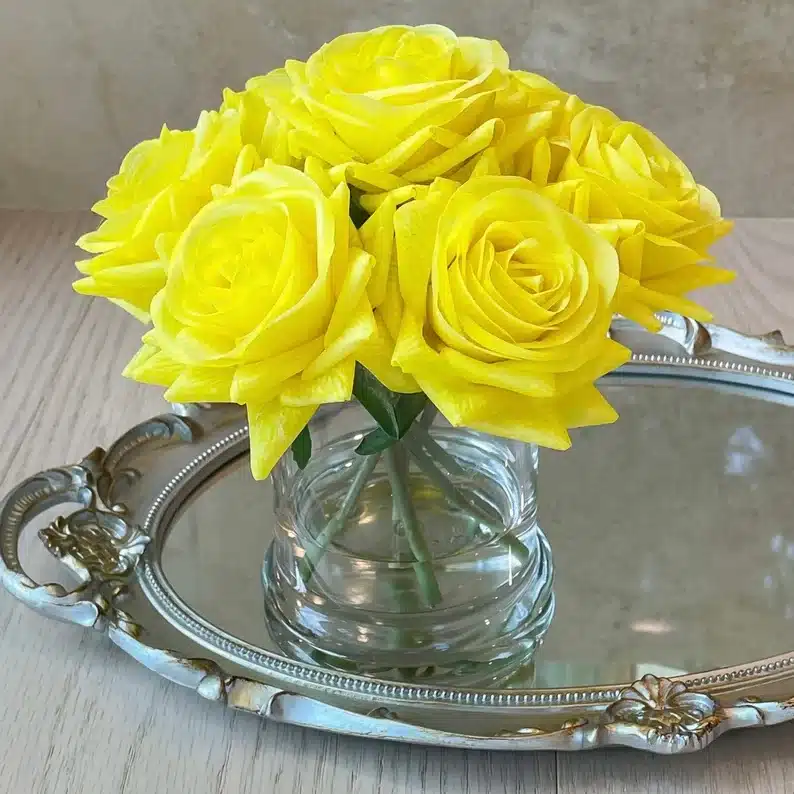 Silver platter with a clear jar on it with yellow roes in it. 