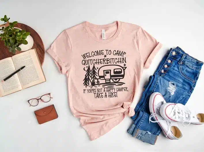 Light pink t-shirt with black font that says welcome to camp quitcherbitchin with a camper trailer. 