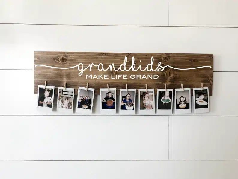 Wooden sign with white font that says "Grandkids make life grand" with clothespins and photos of grandkids attached to each clothespin. 