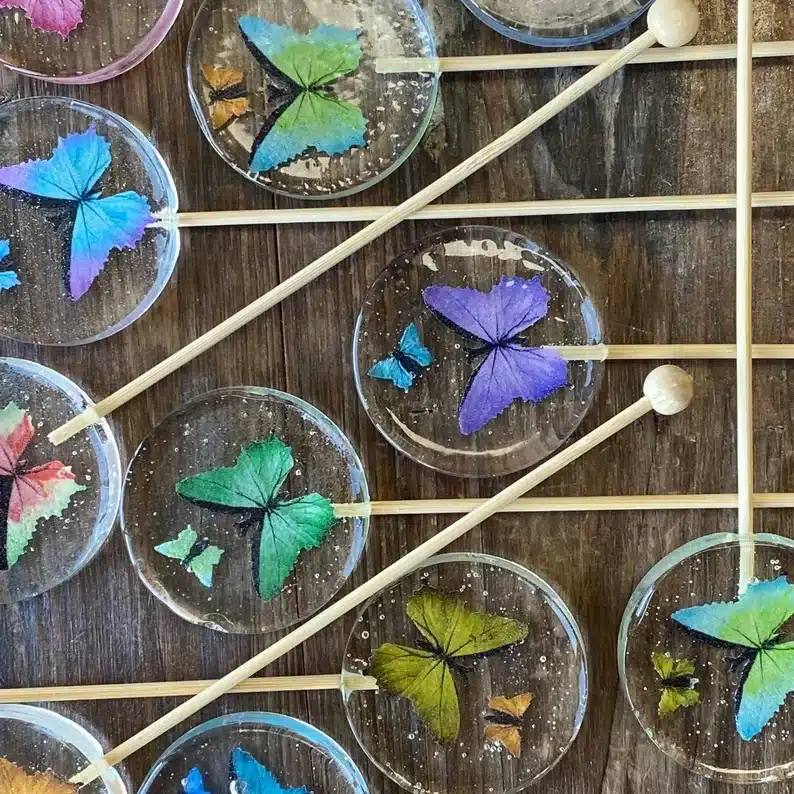 Many clear round lollipops with colorful butterflies inside on a wooden stick. 