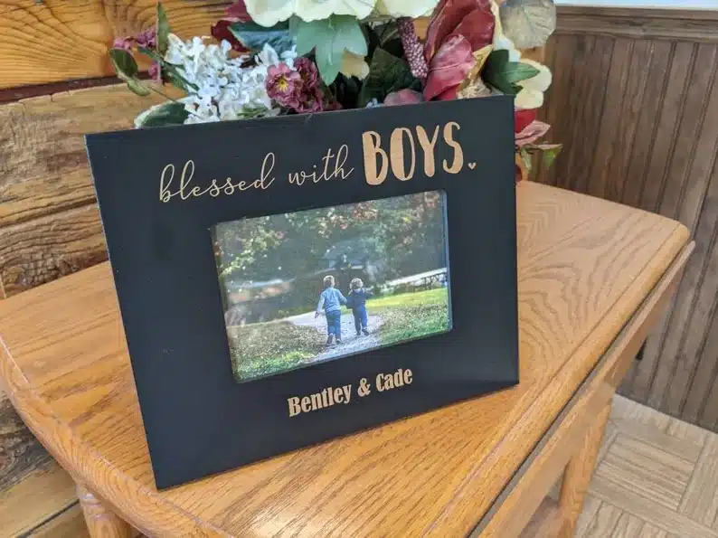 Black picture frame with gold font that says "Blessed with boys" at the top and "Bentley & Cade" at the bottom. A photo of two boys in the center. 