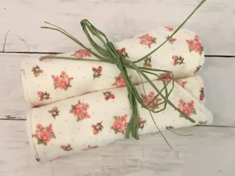 White burp cloth with pink roses all over them wrapped up with green string. 