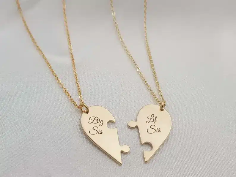 Mother’s Day Gifts for Sisters: Two gold necklaces both with half a heart puzzle piece, one with 