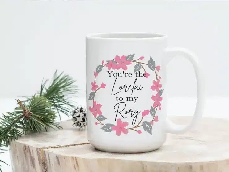 White coffee mug with black font that says You're the Lorelai to my Rory with flowers all around it. 