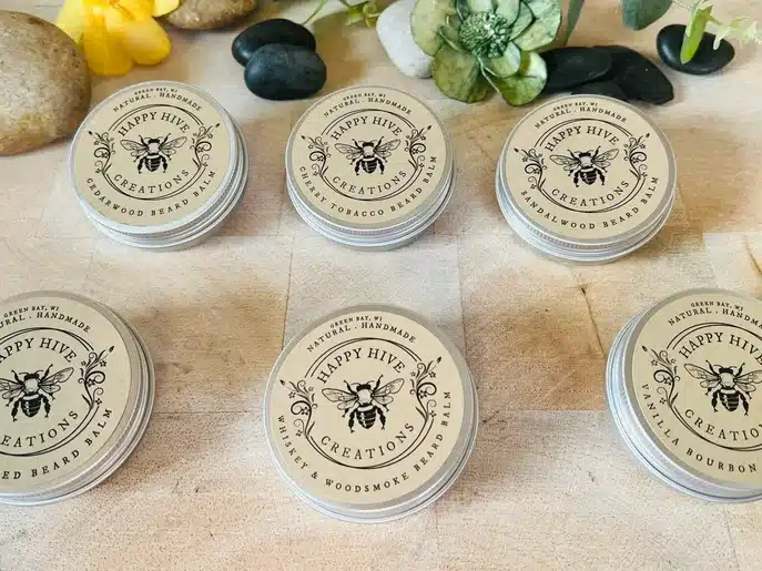 Six small silver beard balm containers with a bee on top. 