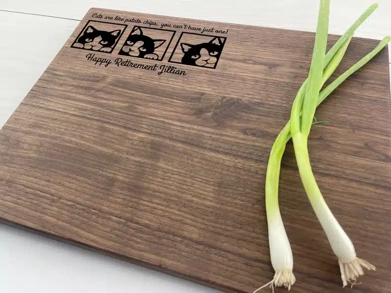 Personalized cutting board thats wooden with cats in the top left corner and green onions on the other. 