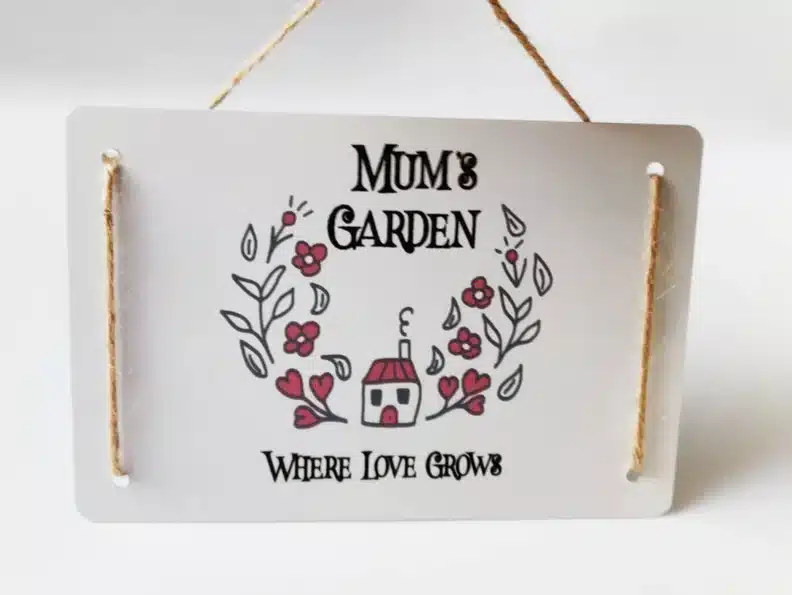 Mother’s Day Gifts for Gardeners: White sign that says MUM's GARDEN in black font with a house and pink flowers around it, below in black font it says WHERE LOVE GROWS. 