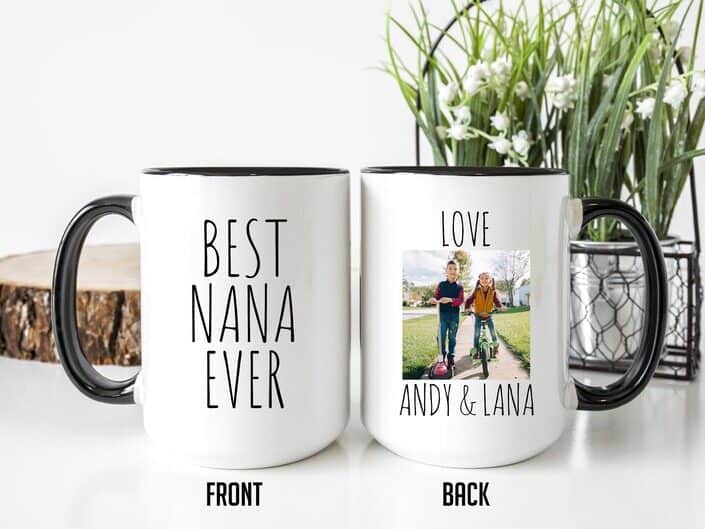 Two white coffee mugs showing the front of a coffee mug that says best nana ever and the back that says love Andy and Lana with a photo of two kids. 