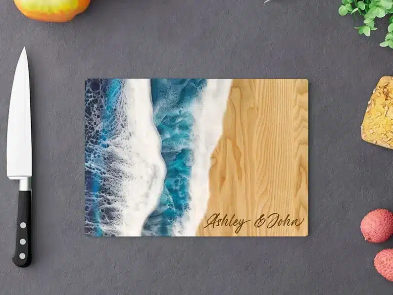 Above view of a wooden cutting board that's half wood and half looks like the ocean, engraved in the corner. 