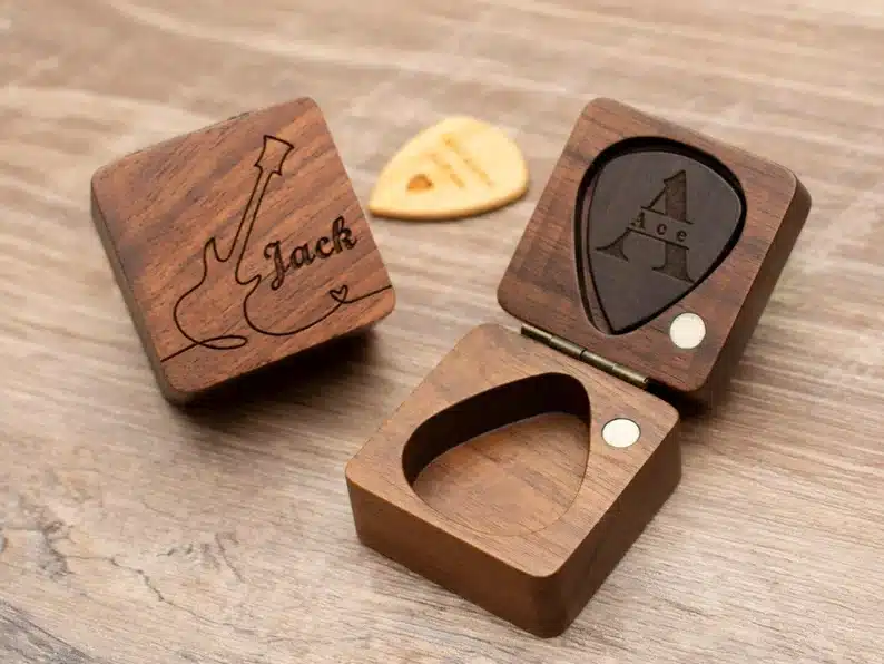 Two small brown boxes to hold guitar picks. one open showing guitar picks inside and the other closed with a guitar engraved on it and jack. 
