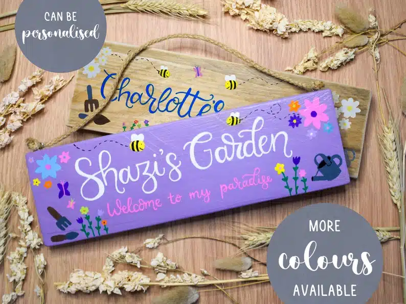 Two wooden signs overlapping one another, one painted purple that says Shazi's garden, and another that says charlotte's garden. 