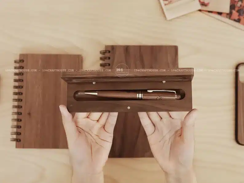Hand holding a wooden box with an engraved wood pen in it. 