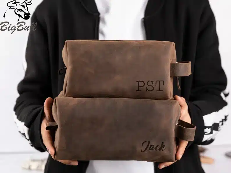 Man holding two brown personalized toiletry kit, one smaller than the other. 