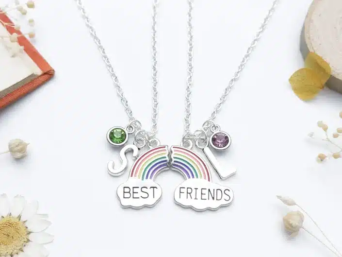 Two silver necklaces each with an initial, birth stone charm, and half a rainbow, one says BEST and one said FRIENDS. 