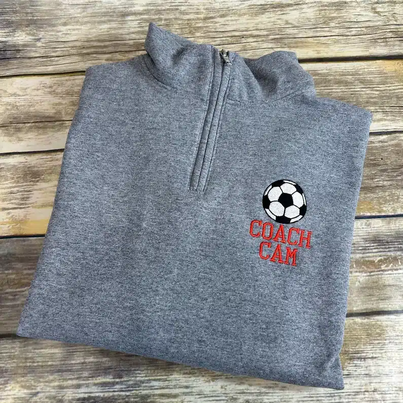 Light grey zip up hoodie with a soccer ball on it with COACH CAM in red. 