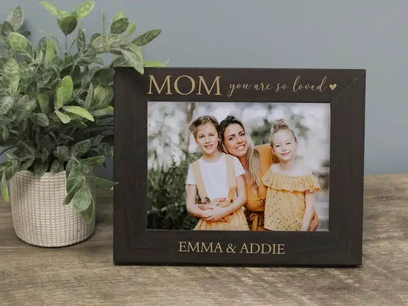 Mother's Day Gifts for 70 Year Olds - Black frame with gold font that  says Mom you are so loved at the top and Emma & Addie on the bottom. A photo of a mom and two girls in the frame. 