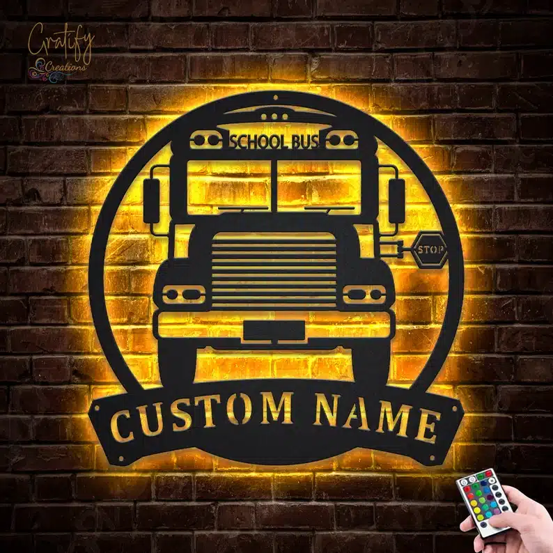 Brick wall with a black metal cut out of a school bus that says CUSTOM NAME below it, all lit up yellow around it. 
