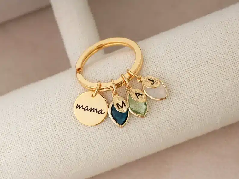 Gold keychain with circle charm that says MAMA and three birthstone charms hanging with each initial of child on top. 