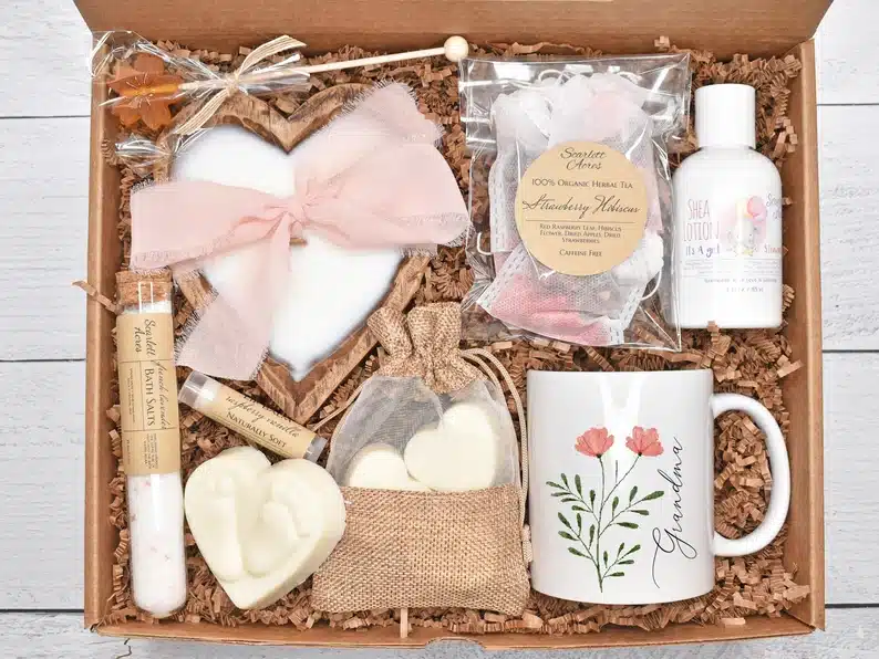 Open box with spa type products with a white coffee mug, bath bombs, lap balm, and lotion. 