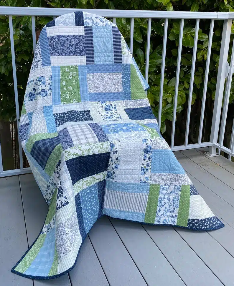 Blue, light green, and dark blue lap quilt with flower, trips, and different patterned patches. 