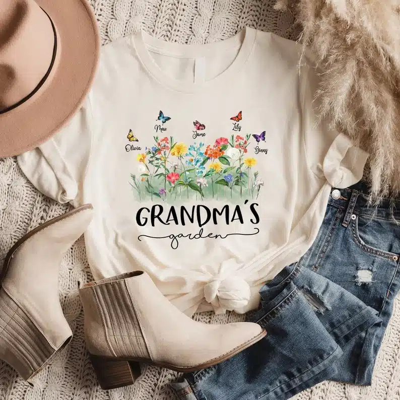 White t-shirt with black font that says Grandma's with flowers and butterflies on it. 