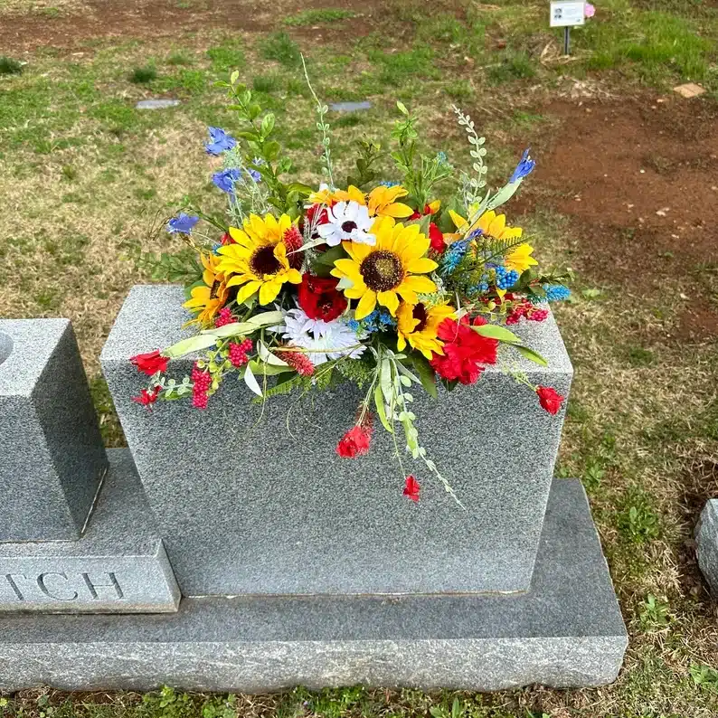 Gravestone with flowers on top, red roses, sunflowers, and white flowers. 