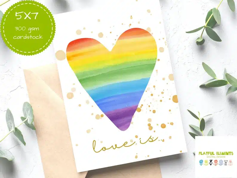 Beautiful Cards for a Gay Wedding: white card with gold bubbles all over that says LOVE Is below a rainbow colored heart. 