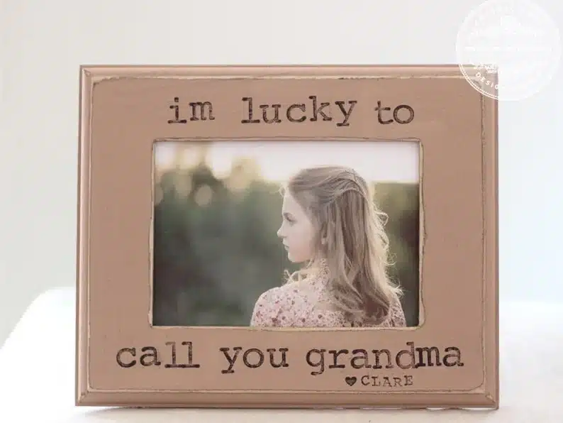 Light brown frame with black font that says I'm lucky to call you grandma love Clare. With a photo of a little girl in it. 