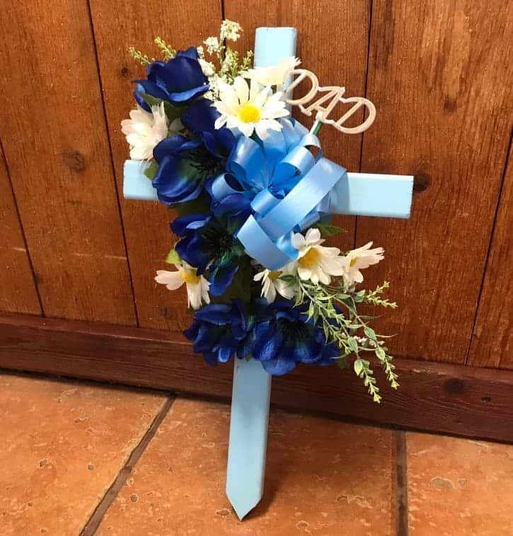 White cross with blue ribons and fake flowers on it.