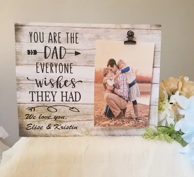 Wooden sign with the saying"you are the dad everyone wishes they had we love you, Elise & Kristin" with a photo of a man and two kids beside. 