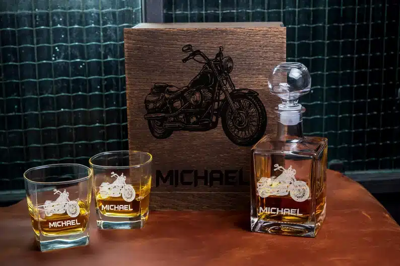 Two whiskey glasses and a decanter set with a engraved motorcycle on it. 