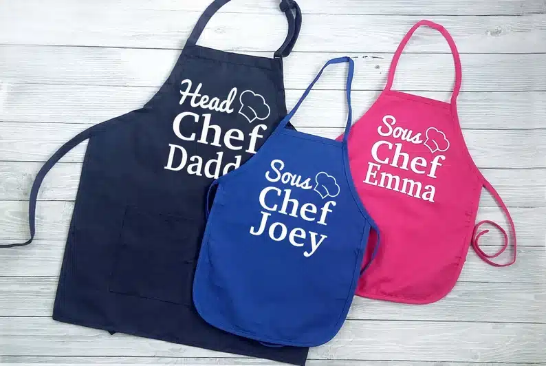Large navy apron that says Head chef daddy and a smaller blue and pink apron that says sous chef joey and sous chef Emma. 